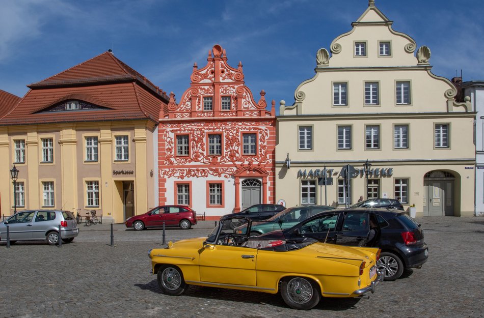 Marketplace scene with beautiful red half-timbered house in the background and in front a yellow older car