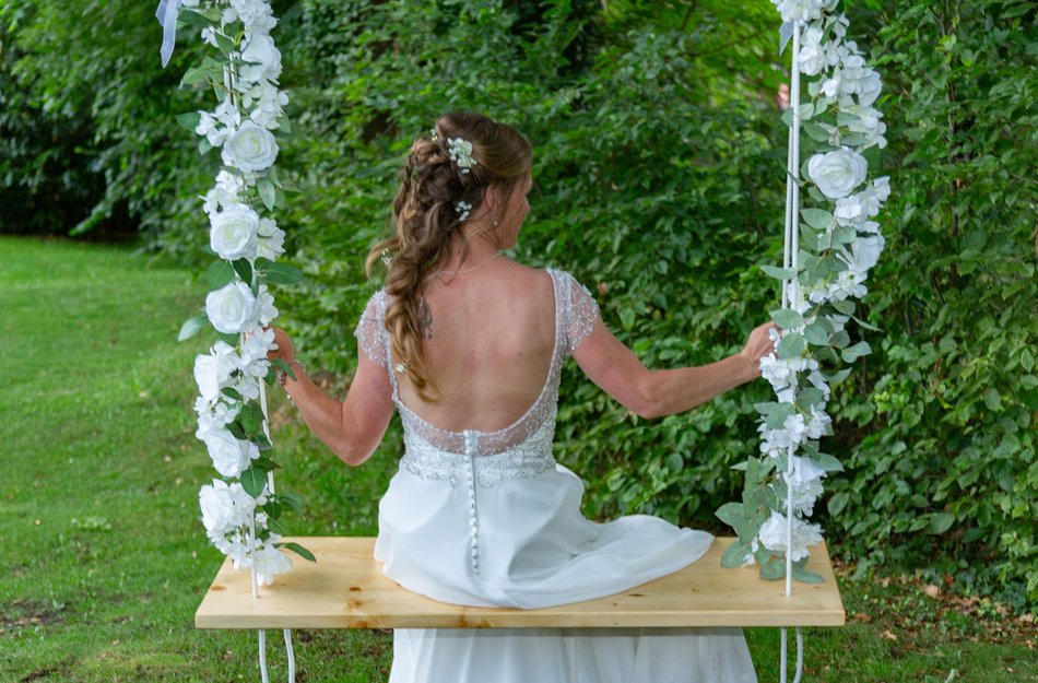 Frau in Hochzeitskleid auf geschmückter Schaukel