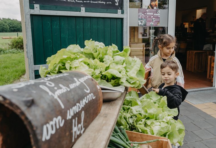 Kinder stehen vor Hofladen in der Auslage große Kohlköpfe und Salate
