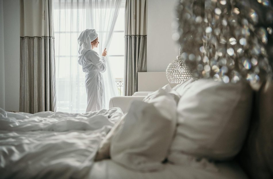 Frau steht im weißen Bademantel an Fenster in Hotel