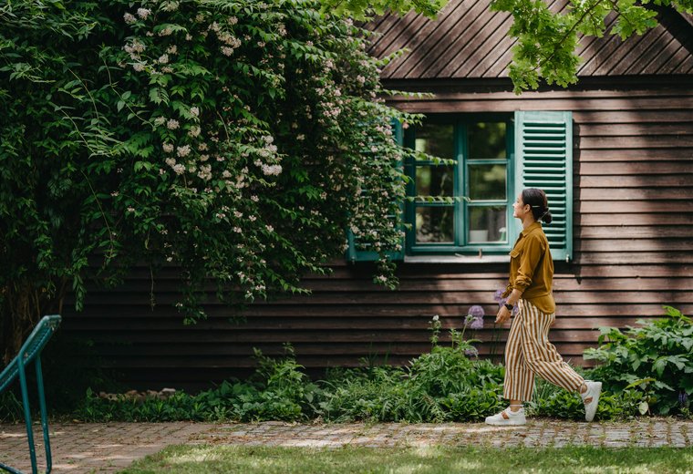 Woman walking along in front of house overgrown with ivy
