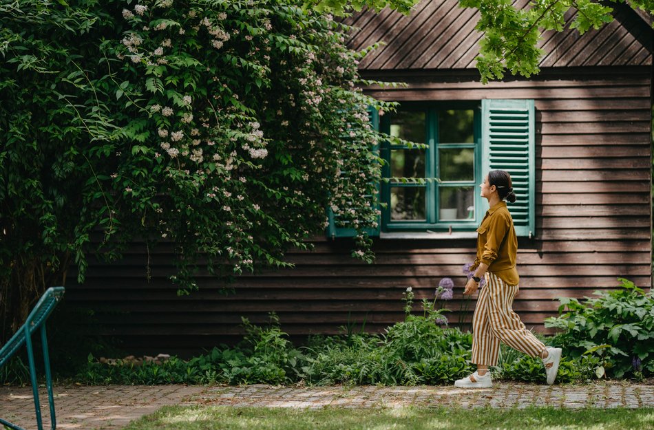 Woman walking along in front of house overgrown with ivy