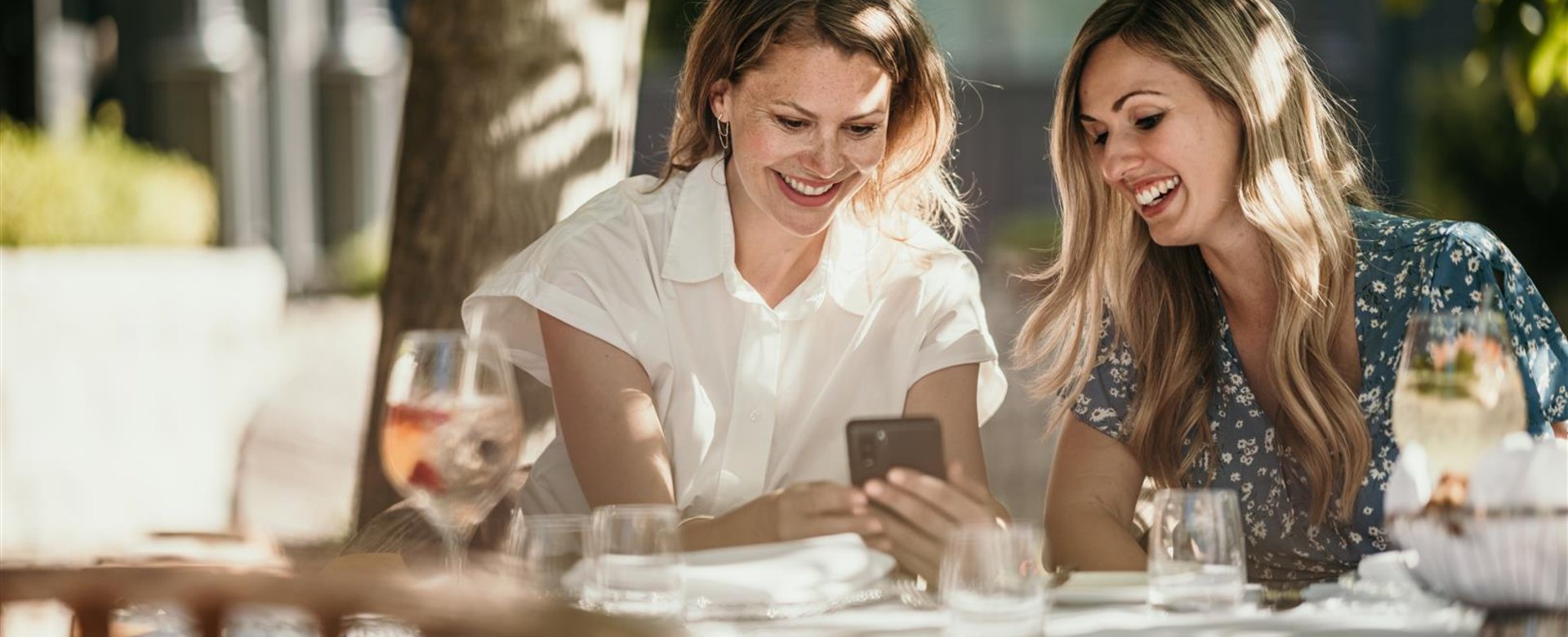 2 Frauen am Mittagstisch schauen auf Handy